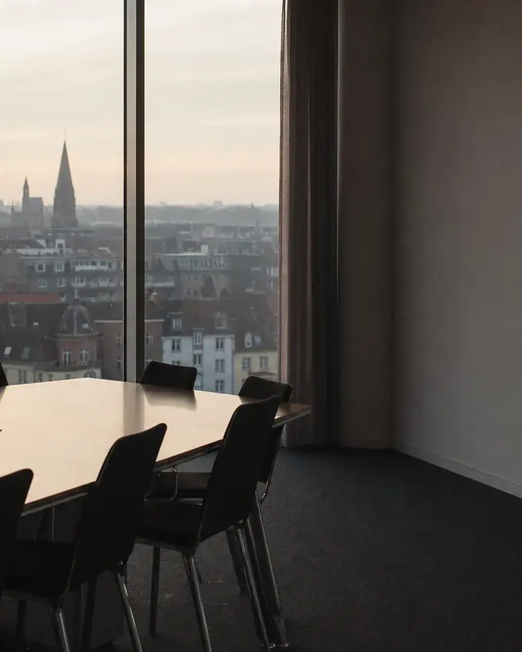 Ein Sitzungssaal mit langem Tisch und Blick auf eine Stadt mit Kirchturm